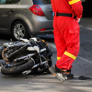 A man in red overalls stands by a motorcycle, damaged by a car collision. This image represents a motorcycle accident in Louisiana. - Whitley-Sebti Law